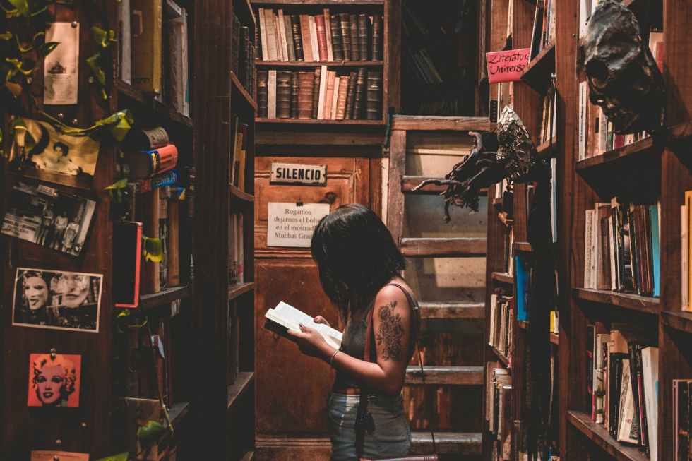 woman standing in library room while reading book